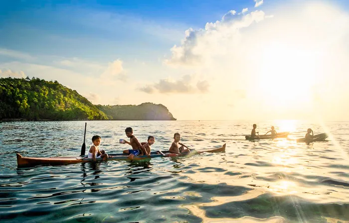 Banda Besar (Great Banda) island, local boys in wooden canoes on the Indian Ocean, silhouetted by the setting sun