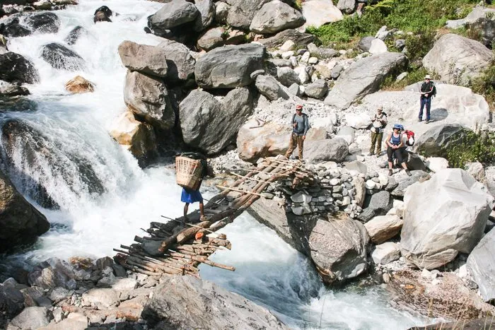A porter crosses a makeshift bridge over a tributary of the Buri Gandaki